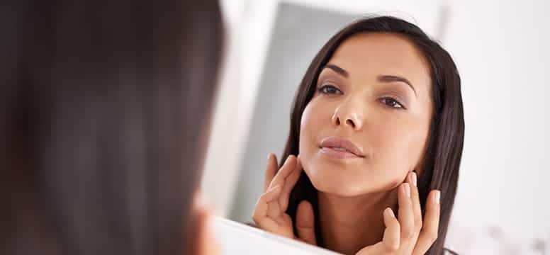 image of a woman looking at her face in the mirror, inspecting her skin