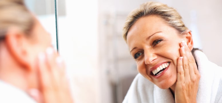 Woman looking at her face in the mirror and smiling after Sciton Laser treatments