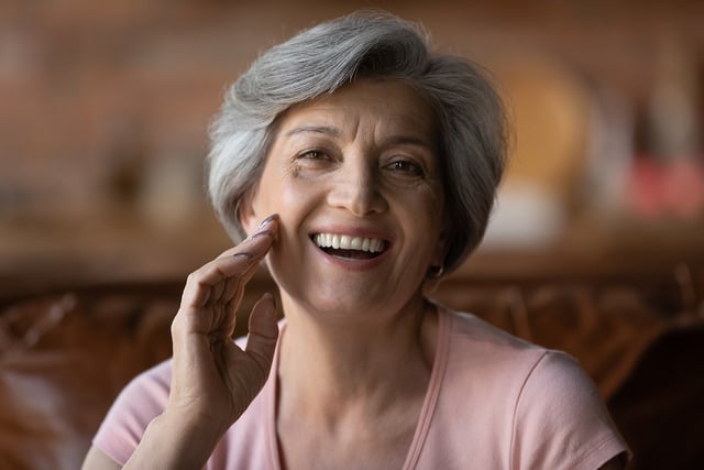 Woman in her 60s smiling touching her skin considering a skin exam