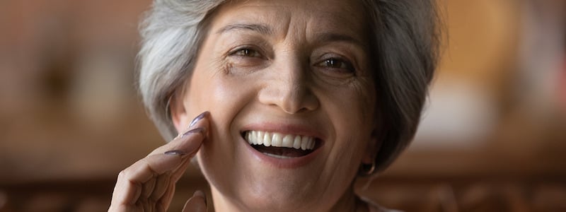 Woman in her 60s touching her face considering getting a skin exam